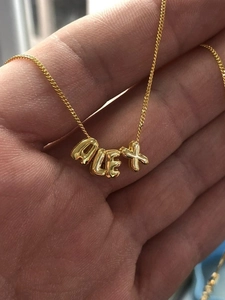 Makroaufnahme des vergoldeten 18K Bubble-Buchstaben ALEX Anhängers in der Hand