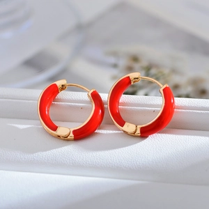 Detail of red and gold enamel hoop earrings on a textured white leather surface