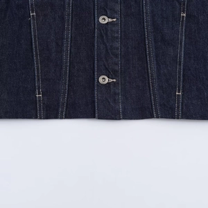 Détail de la veste en jean bleu foncé avec boutons métalliques vintage et coutures blanches