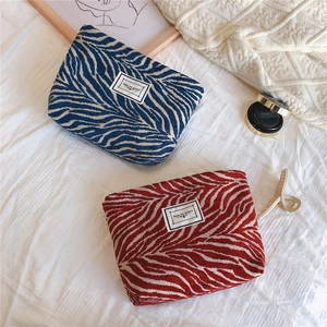 Detailed close-up of navy and brick red chenille makeup bags on a soft bedsheet