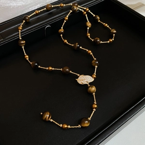 Detailed view of zircon leaf pendant and tiger eye beads on a golden necklace