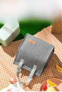 Detail of grey insulated lunch bag with 'Tasty Food' label on a picnic blanket