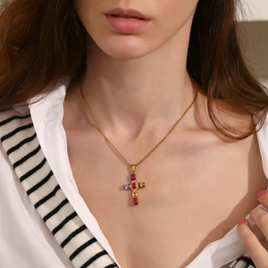 Close-up of golden cross necklace with colorful oval gems worn by a female model