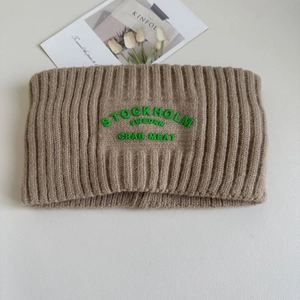 Detail eines kaffeebraunen Strickstirnbands mit grüner Stockholm Sweden Bestickung