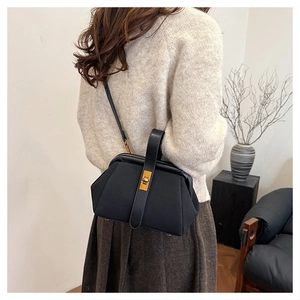 Chic black shell bag with golden buckle shown on shoulder for daily styling