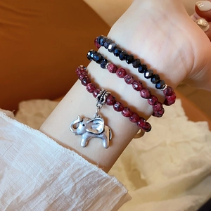 Close-up of triple-layered bead bracelets with silver elephant charm and gemstone texture
