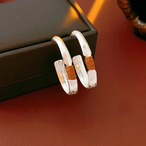 Detail shot of matte silver U-shaped earrings with hand-hammered texture and brown leather wrap