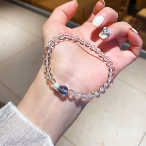 Bracelet en perles de cristal blanc porté au poignet avec perle bleue et breloque