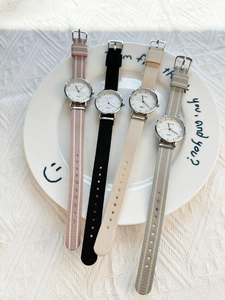 Detail showing four minimalist quartz watches with colorful nylon straps on a white ceramic plate