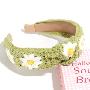 Close-up of a green knitted headband with daisy flower embroidery and a stylish knot