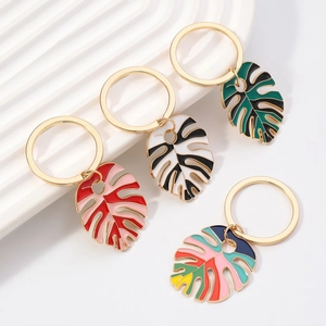 Detailed set of four colorful enamel monstera leaf keychains on white ceramic stand