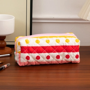 Quilted cotton cosmetic bag with yellow polka dots and red stripes on a wooden desk