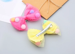 Detail of children's mesh bow hair clip with colorful pom-poms and metal alligator clip
