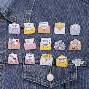 Dettaglio di spille smaltate colorate con frasi motivazionali su giacca di jeans