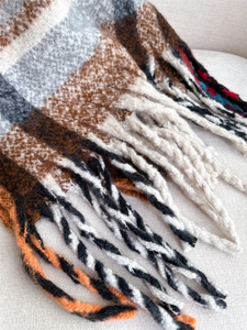 Close-up of thick plaid scarf with brown beige tassels and soft brushed texture