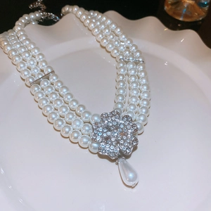 Detail of multi-layer pearl necklace featuring a diamond flower pendant and teardrop pearl