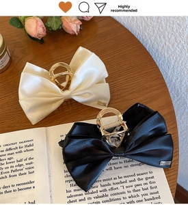 Detail of satin bow hair claws in black and beige on a wooden surface with decor