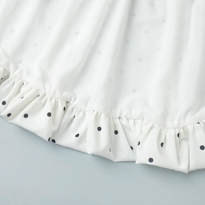 Detailed macro view of white polka dot fabric with delicate ruffled hem and smooth texture