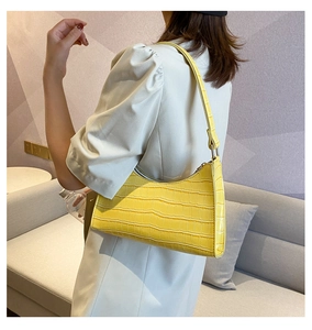 Detailed close-up of bright yellow crocodile pattern underarm bag on female model