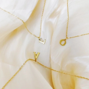 Detailed shot of three gold initial necklaces on white satin background with E O A charms