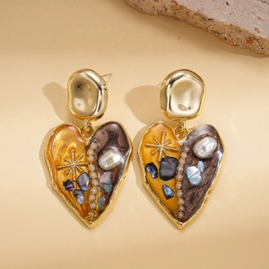 Vintage heart earrings in gold finish with amber resin and pearl details on leather surface