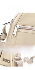 Detail view of beige nylon crossbody bag with metal zipper and wide woven shoulder strap