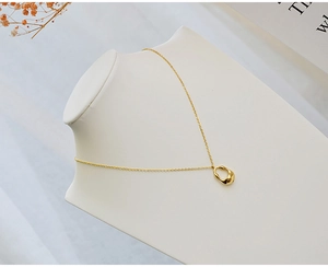 Detailed close-up of a minimalist gold teardrop pendant necklace on a white bust stand