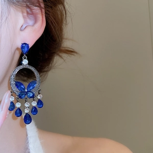 Close-up of elegant blue crystal tassel earrings with butterfly detail worn by a model