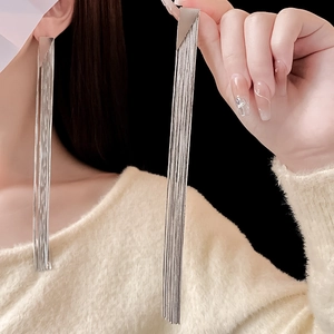 Macro shot of long silver tassel earrings worn by a model against a black background