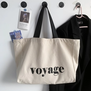 Close-up of beige canvas tote bag with black voyage lettering and shoulder straps