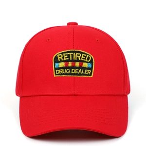 Detail of red cotton baseball cap featuring Retired Drug Dealer embroidered patch
