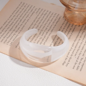 Detailed close-up of translucent white acrylic open bangle on a vintage book