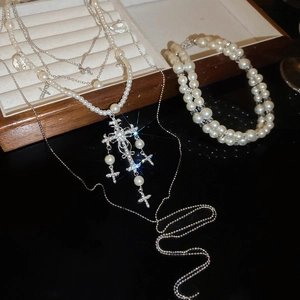 Detailed view of luxury layered pearl necklace with rhinestone cross pendants on black surface