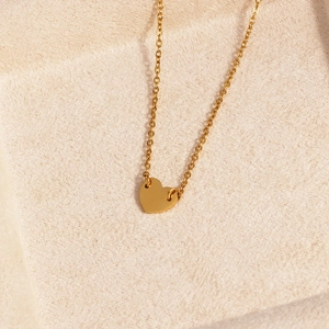 Gros plan du collier doré avec pendentif cœur minimaliste sur fond de tissu beige
