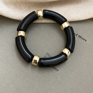 Detail of minimalist black acrylic segment bracelet with golden metal ring accents