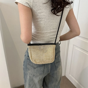 Borsa a secchiello a tracolla in paglia intrecciata con cinturino nero indossata da modella