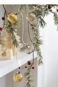 Close-up of elegant LED string lights with striped metallic glass bulbs on pine branches