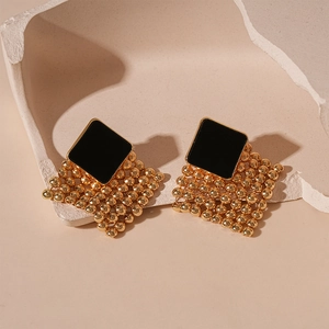 Detail of geometric woven earrings with black squares and gold metallic beads on stone