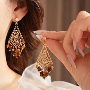 Ethnic style gold hollow earrings with tiger eye beads and orange tassels on a model