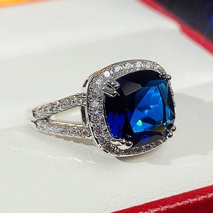 Macro shot of silver ring with blue square gemstone in a red jewelry box lining
