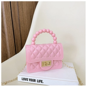 Pink jelly handbag with beaded handle and gold chain strap on a white book surface
