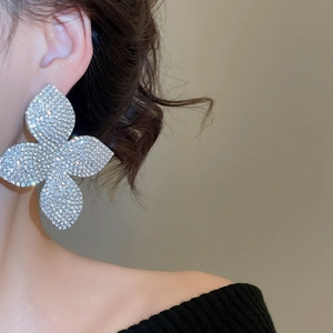 Dettaglio di orecchini a fiore argentati con pavé di strass indossati da una modella