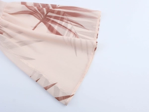 Close-up of pink chiffon fabric featuring brown palm leaf prints and fine rolled hem detail