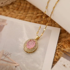 Detail of gold-plated oval pendant with pink stone and zircon on a magazine background