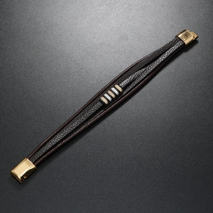 Detail of multi-layer brown braided leather bracelet with mixed metal charms and gold clasp