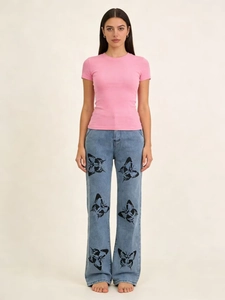 Détail du jean bleu large avec motifs de papillons noirs symétriques sur le bas des jambes
