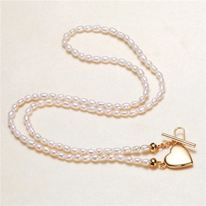 Detail of double-layer pearl necklace featuring a gold heart pendant and OT toggle clasp