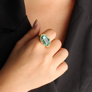 Vintage gold ring with large oval green gemstone on finger with black suit backdrop