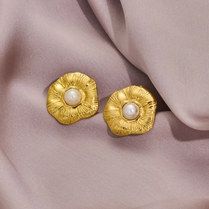 Close-up of golden petal flower earrings with white pearl centers on silk background