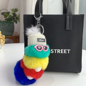 Colorful plush caterpillar keychain with white knit hat and pink glasses on black tote bag